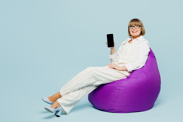 Wall Mural - Full body employee business woman 50s wear white classic suit glasses formal clothes sit in bag chair use blank screen mobile cell phone isolated on plain blue background. Achievement career concept.