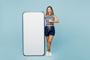 Sticker - Full body young woman she wears striped tank shirt casual clothes point on big huge blank screen mobile cell phone smartphone with workspace area isolated on plain pastel light blue cyan background.