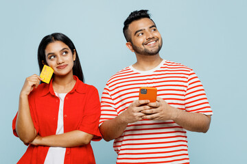 Wall Mural - Young minded couple two friend family Indian man woman in red casual clothes t-shirt use mobile cell phone credit bank card shopping online book tour together isolated on plain blue color background
