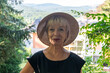 © Anelo - Portrait of an elderly happy woman, 60-65 years old, wearing a straw hat, against the background of a European country house.