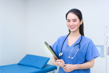 Professional young Asian woman doctor standing smiling in medical uniform blue lab shirt holding patient documents in hand examination room in the hospital. Health care concep.