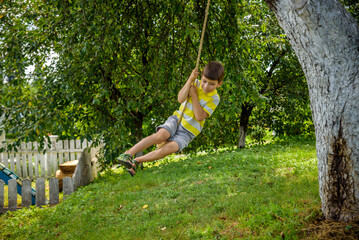 Wall Mural - Happy little boy is having fun on a rope swing which he has found while having rest outside city. Active leisure time with children