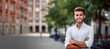 © Creative Clicks - A young man in a city, looking at the camera, a confident businessman with arms crossed, smiling outdoors.