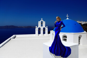 Wall Mural - Elegant woman in blue long sequin dress is posing outdoor in luxury resort in Santorini. Female model in amazing long dress. Vogue. Couture.