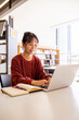 © Austockphoto - Young adult asian woman at the library studying and using her laptop