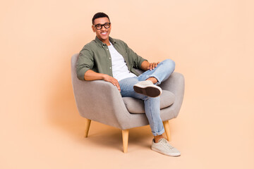 Canvas Print - Full size photo of cheerful pleasant man wear stylish shirt denim pants sit in armchair relaxing isolated on beige color background