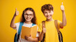 Two Cheerful happy young small schoolgirl and schoolboy make fingers thumbs up smile isolated on yellow color background.Created with Generative AI technology.