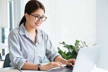 Poster - Cheerful business lady working on laptop in office, Asian happy beautiful businesswoman in formal suit work in workplace. Attractive female employee office worker smile.