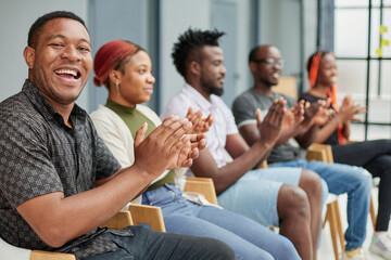 Group of men and women sit in a row and applaud a man who puts forward an idea or says something.