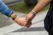 LGBTQ couple holding hand with rainbow-colored bracelets on their wrists outdoors