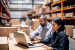 © InputUX - Warehouse managers immersed in work on a laptop, efficiently coordinating logistics, shipping, and inventory for business fulfillment.