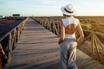 Wall Mural - Back view of fashionable girl with white summer hat walking on the beach. Summer holidays and relax on the beach