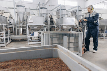 Wall Mural - Man loader in uniform working trolley with cedar nuts pine in warehouse. Industrial manufacturing factory