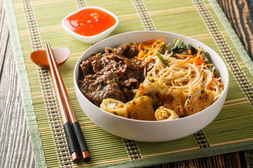 Poster - Vietnamese beef noodles salad bun bo xao is filled in fresh herb, savory beef, vegetables and fried spring rolls closeup on the table. Horizontal