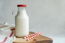 Raw Cow Milk In Vintage Bottle On Cutting Board Near Drinking Straws And Napkin