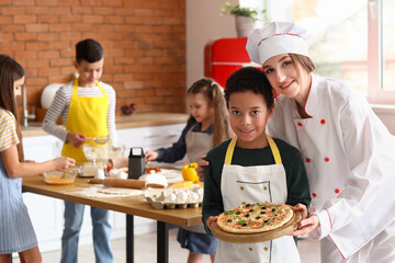 Wall Mural - Female chef with little boy and prepared pizza after cooking class in kitchen