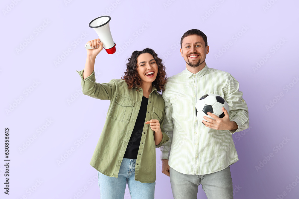 Young couple with soccer ball and megaphone on lilac background