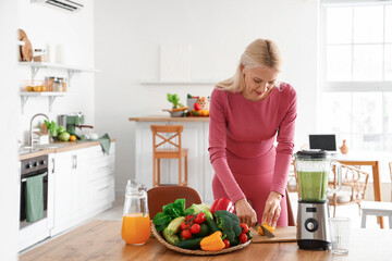 Poster - Sporty mature woman cutting lemon for healthy smoothie in kitchen