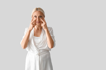 Poster - Mature woman doing face building exercise on light background