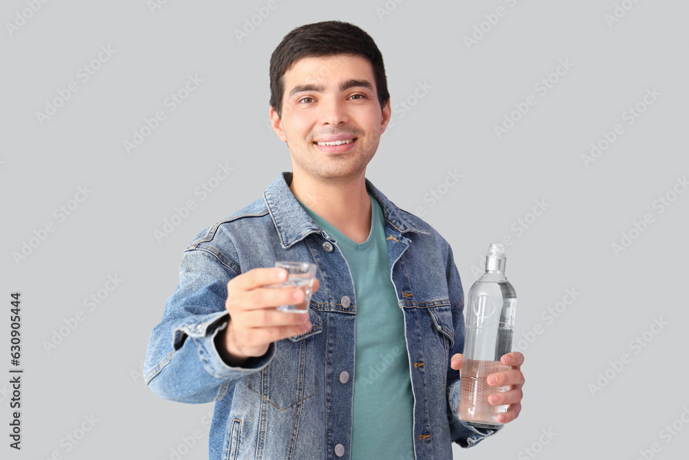 Young man with glass and bottle of vodka on light background