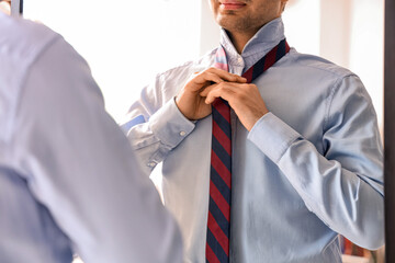 Sticker - Young businessman tying his necktie in front of mirror at home, closeup