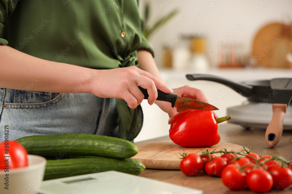 Young woman cutting bell pepper in kitchen, closeup