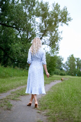 Portrait of blonde woman in a park. Young woman in blue vintage dress. Female walks in summer nature barefoot . Long hair.