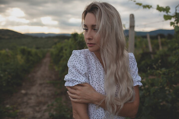 The beautiful blond woman walking in the vineyard. The female wearing the dress and enjoy the landscape