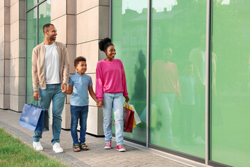 Wall Mural - Family shopping. Happy parents and son with colorful bags near mall outdoors