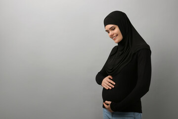 Portrait of pregnant Muslim woman in hijab on light gray background, space for text