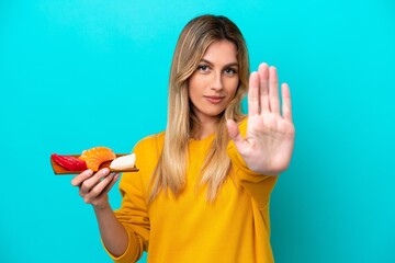 Canvas Print - Young Uruguayan woman holding sashimi isolated on blue background making stop gesture