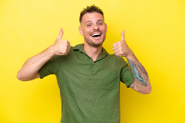 Poster - Young caucasian handsome man isolated on yellow background giving a thumbs up gesture