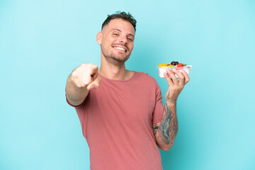 Wall Mural - Young caucasian man holding a bowl of fruit isolated on blue background pointing front with happy expression