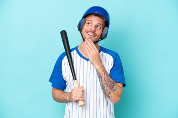 Wall Mural - Baseball player with helmet and bat isolated on blue background looking up while smiling