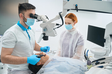 Wall Mural - Young dentist in the clinic fills a tooth for client