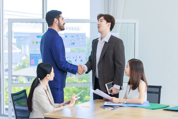 Millennial Asian Indian multinational professional successful businessmen  in formal suit standing shaking hands greeting say hello together in conference meeting room with businesswomen colleagues