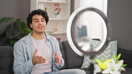 Sticker - Young latin man sitting on sofa recording video tutorial at home