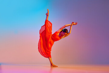 Dynamic image of young talented, artist woman in elegant red dress dancing against gradient multicolored background in neon light. Concept of modern dance style, hobby, art, performance, lifestyle, ad