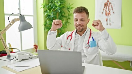 Canvas Print - Young man doctor using laptop working with winner gesture at clinic