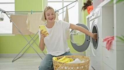 Wall Mural - Young blonde woman using smartphone washing clothes smiling at laundry room