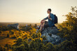 © baranq - Travel and hiking concept. Adult man with backpack sitting on the edge of rock enjoying landscape during sunset