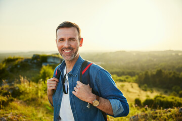 Portrait of happy adult man hiking with backpack during sunny day