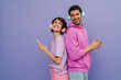 © Drobot Dean - Smiling couple in headphones using smartphones while standing back to each other isolated over purple wall