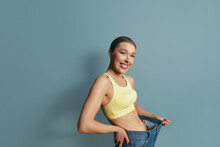 Woman Shows Her Weight Loss,  Wearing On Jeans . Isolated On Blue Background. Diet Concept. Weight Loss
