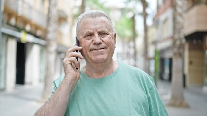 Wall Mural - Middle age grey-haired man smiling confident talking on the smartphone at street