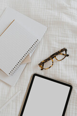 Tablet with blank copy space screen, glasses, sheets for notes on white muslin fabric. Flat lay, top view