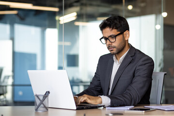 young serious and focused businessman at workplace typing on computer, arab man in business suit sit