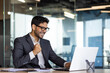 © Liubomir - Young successful arab businessman at workplace inside office, man in business suit with laptop celebrating victory received online win notification, boss winner rejoices and celebrates triumph.
