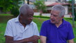© Marco - Two older diverse friends conversing at park bench. A retired African American and a caucasian senior people talking outside