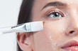 Beautiful young white woman applying cleansing gel to her facial skin using brush